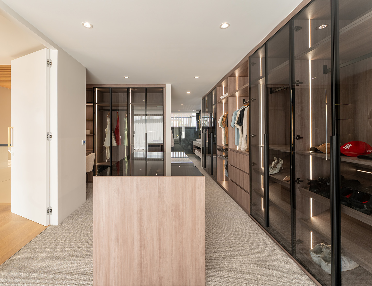 Premium custom walk in wardrobe with elegant tinted glass doors and island.
