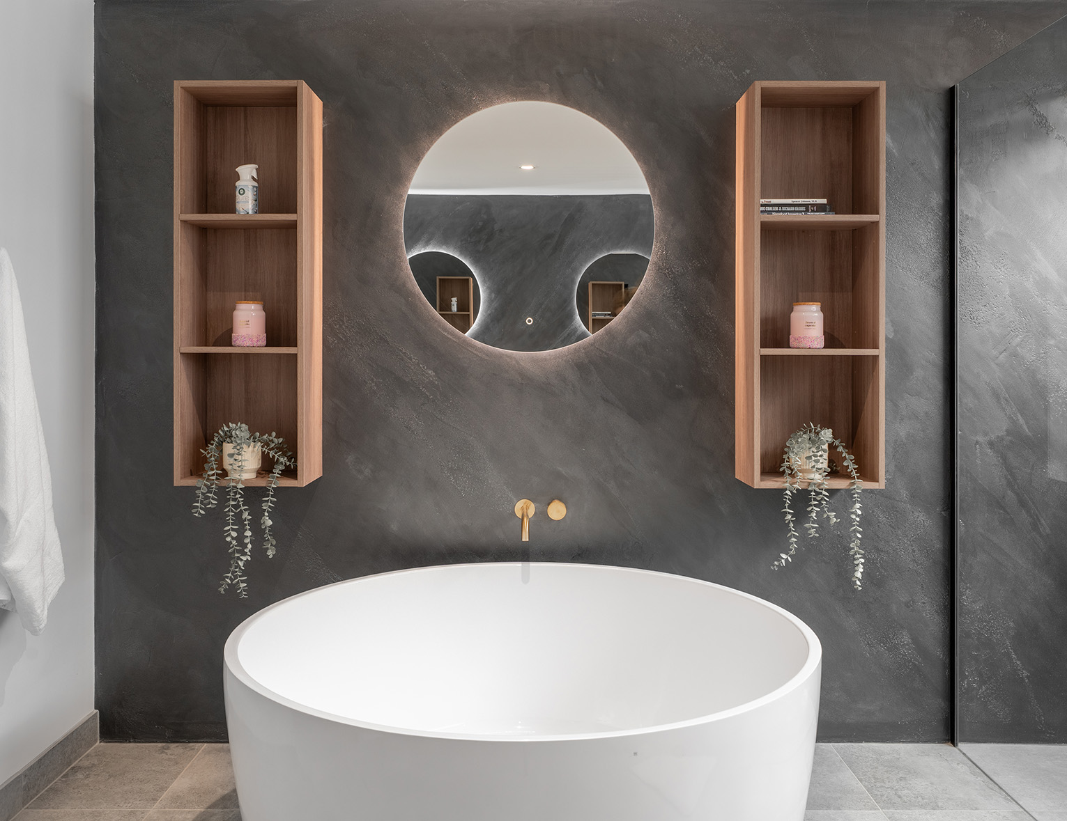Modern bathroom, slate feature wall, round mirror centred between two custom wooden shelving units. Large round bathtub makes a bold statement, front and centre.