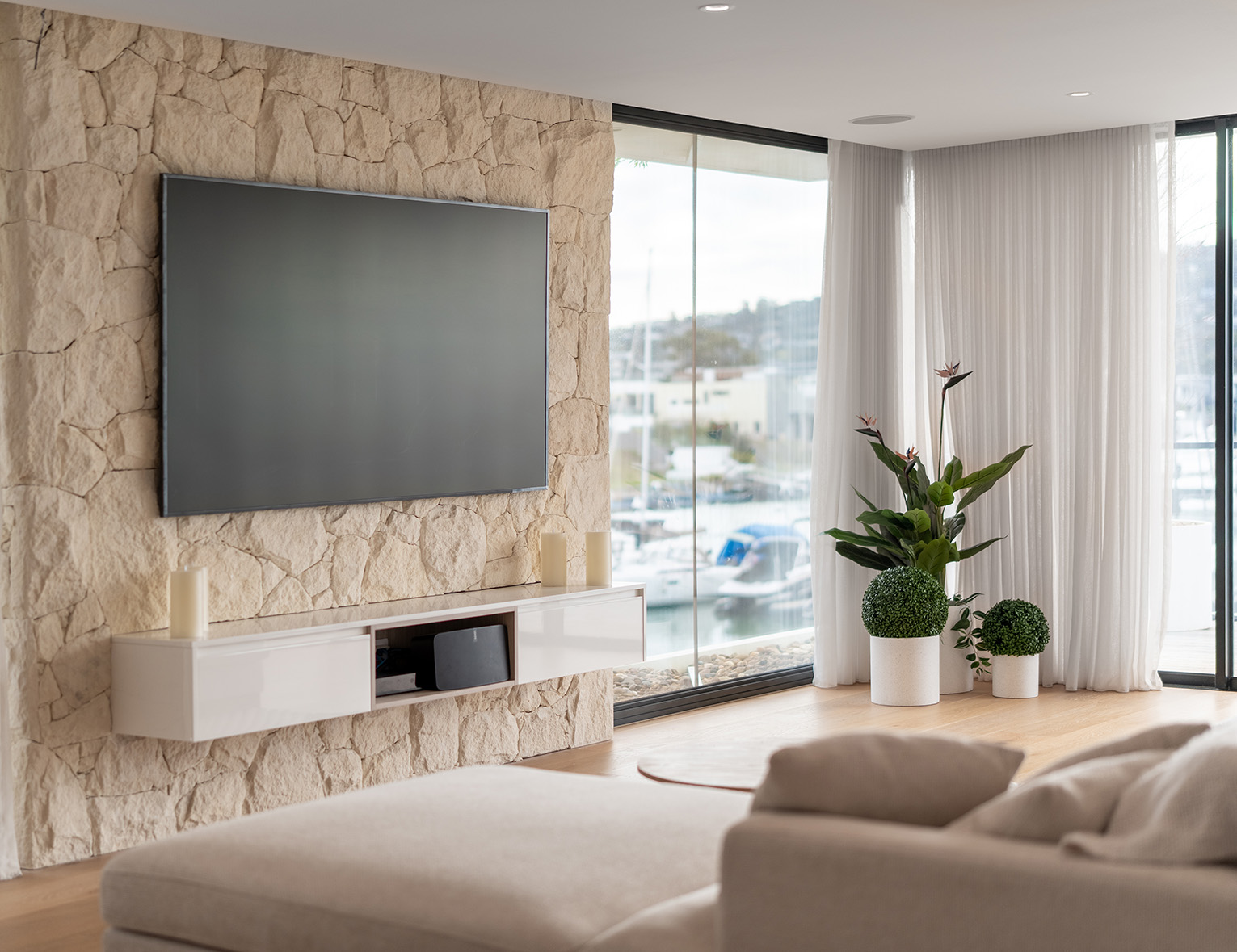 Luxurious stone feature wall, wall-mounted television, sleek custom entertainment cabinets, and black steel corner floor-to-ceiling windows.