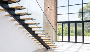 Freestanding steel staircase, with beautiful floating wooden treads, creating a dramatic focal point in this modern, industrial Mount Eliza home. Steel entrance door and frosted windows create the design intent from the very first impression